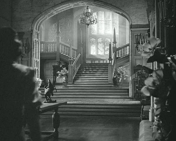 A black and white photo of an elaborate manor entry hall, including an impressive staircase.
