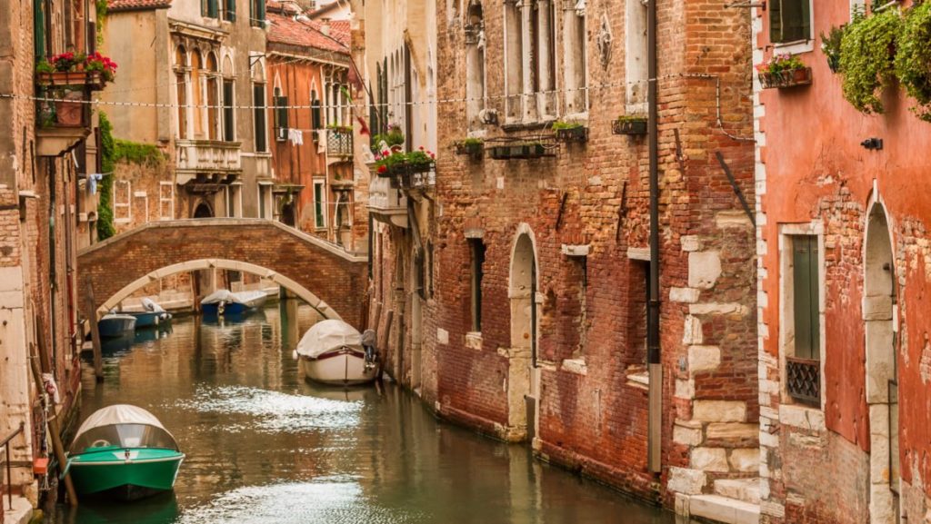 A green boat on a Venice-style canal surrounded by brick buildings.